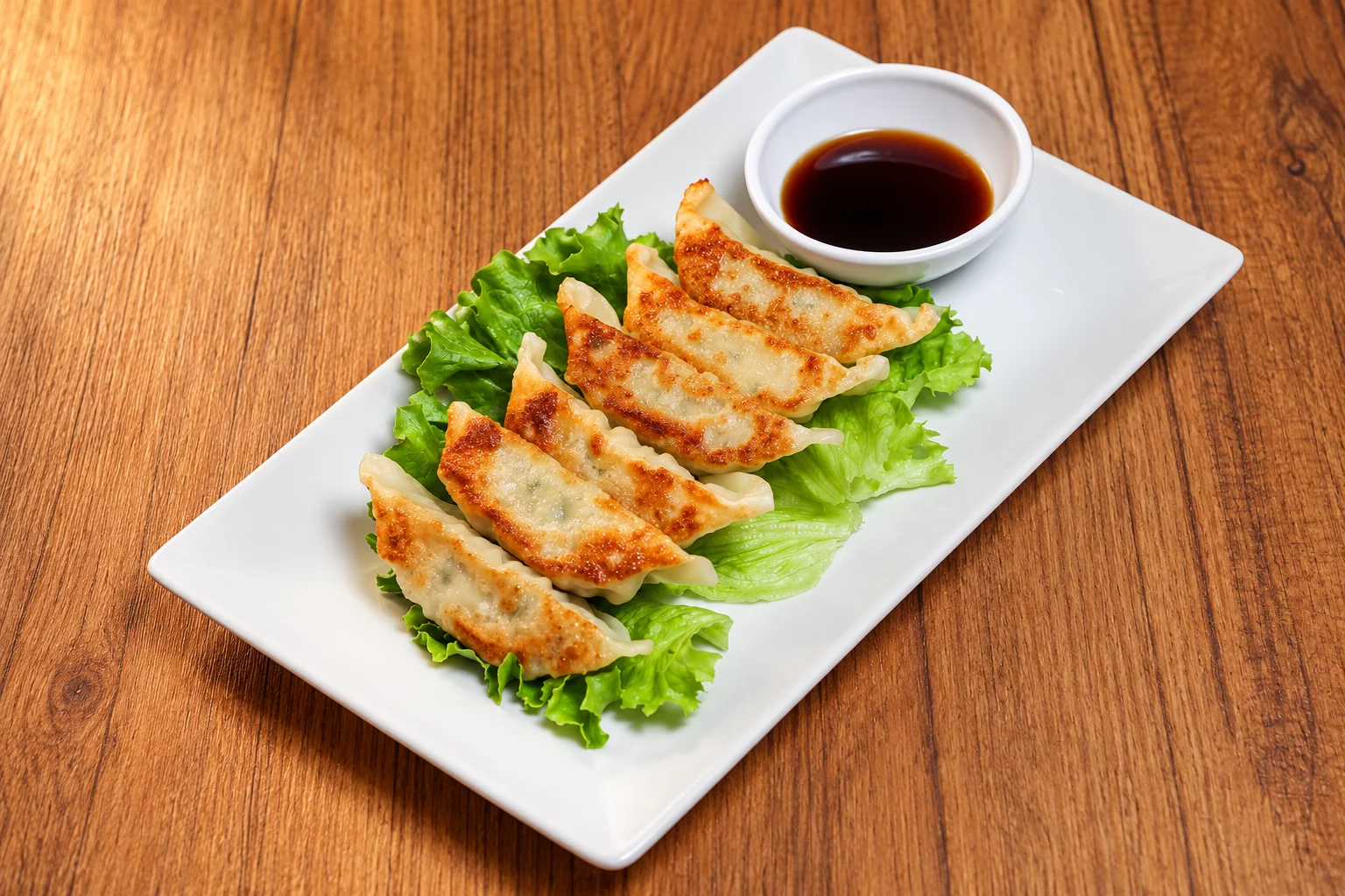 Raviolis grillés au poulet sur salade, assiette blanche rectangulaire, table en bois