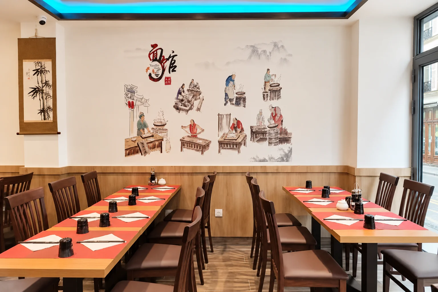 Salle du restaurant : fresque murale, tables en bois et sets de table rouges
