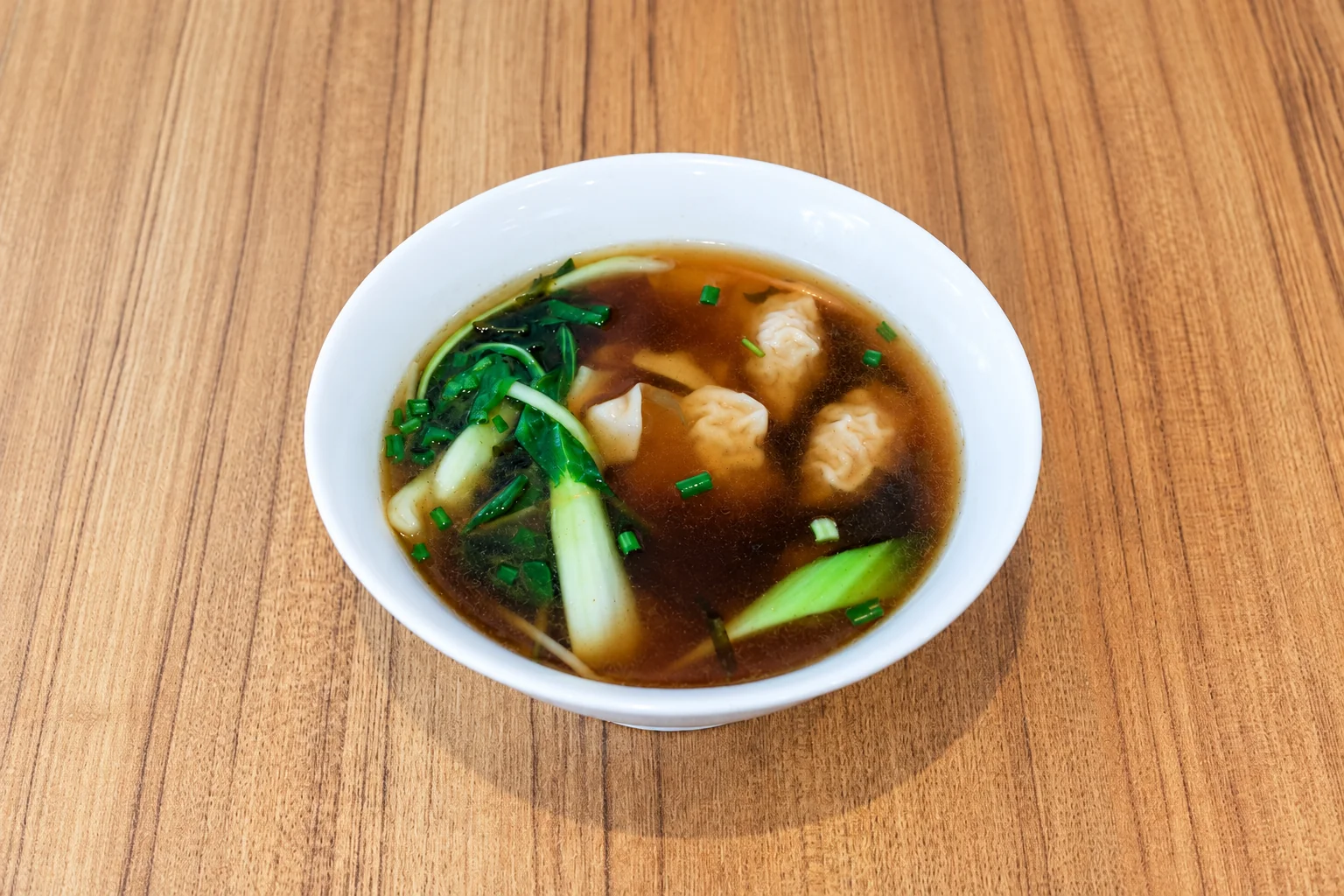 Soupe aux raviolis chinois dans un bol blanc, table en bois